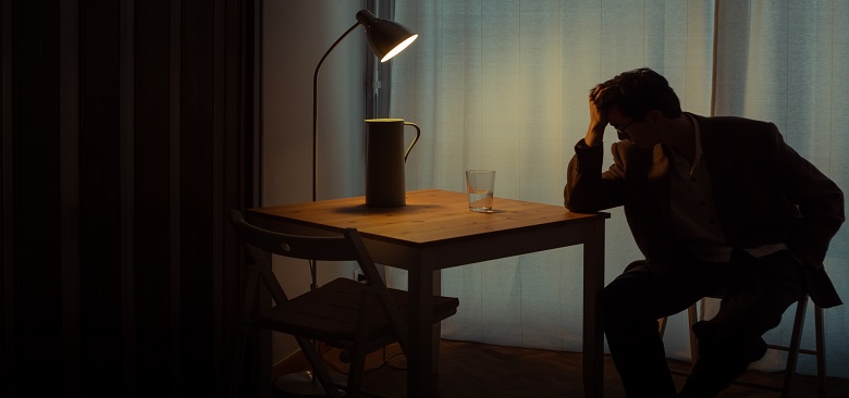 Työuupumuksesta kärsivä mies istumassa pöydän ääressä pimeässä